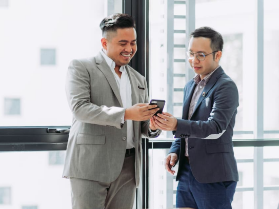 photo of two business men talking and looking at phone