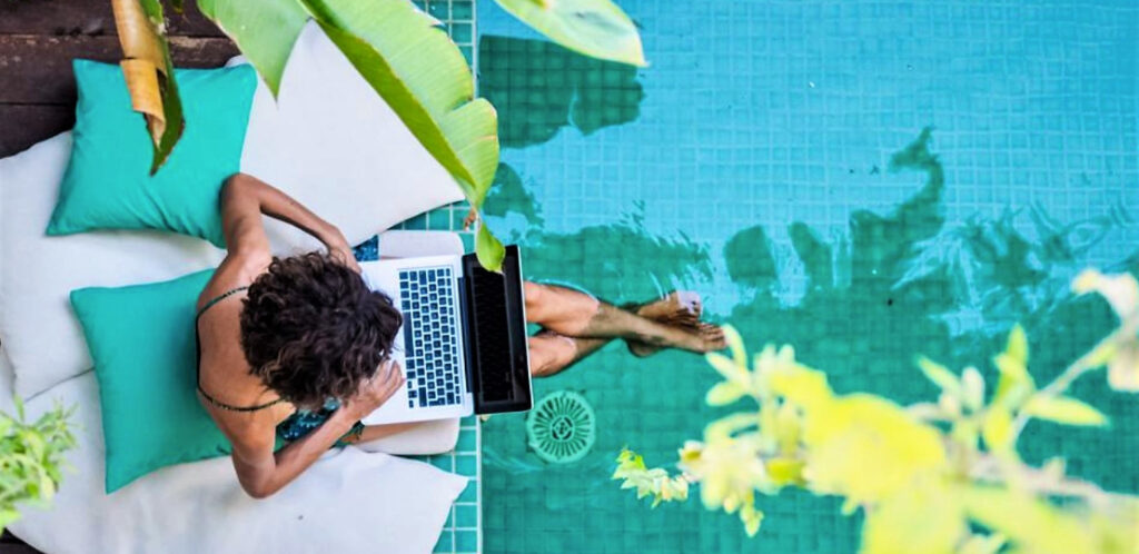 photo of a woman working on a lap top with her toes in a pool