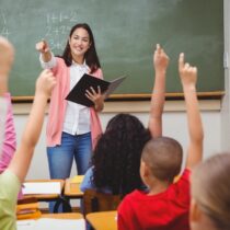 photo of teacher in front of class with students with raised hands