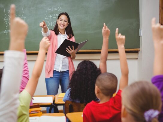 photo of teacher in front of class with students with raised hands